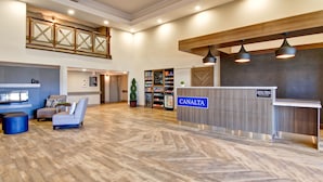 A spacious lobby with a reception desk labeled "CANALTA," a seating area with a blue ottoman, and a herringbone-patterned floor. - Canalta Hotel Brooks (Brooks)