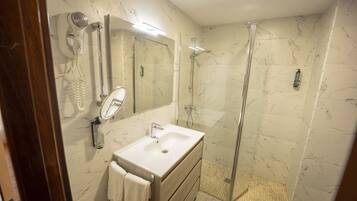 Un baño con pared de mármol, un lavabo blanco, un espejo, un secador de pelo y una ducha con mampara de vidrio.