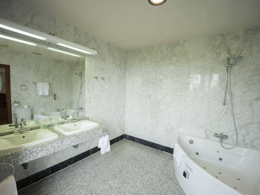 Un baño con dos lavamanos, un espejo grande, una bañera y paredes de mármol.