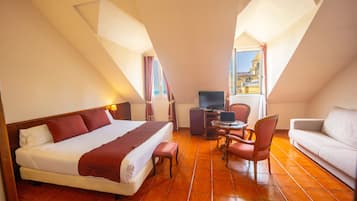 A hotel room with a bed, a desk with a computer, a chair, a sofa, and a TV.