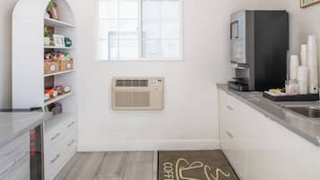 Eine moderne Küche mit weißen Schränken, einer eingebauten Klimaanlage, einer Kaffeemaschine und einem Fenster.
