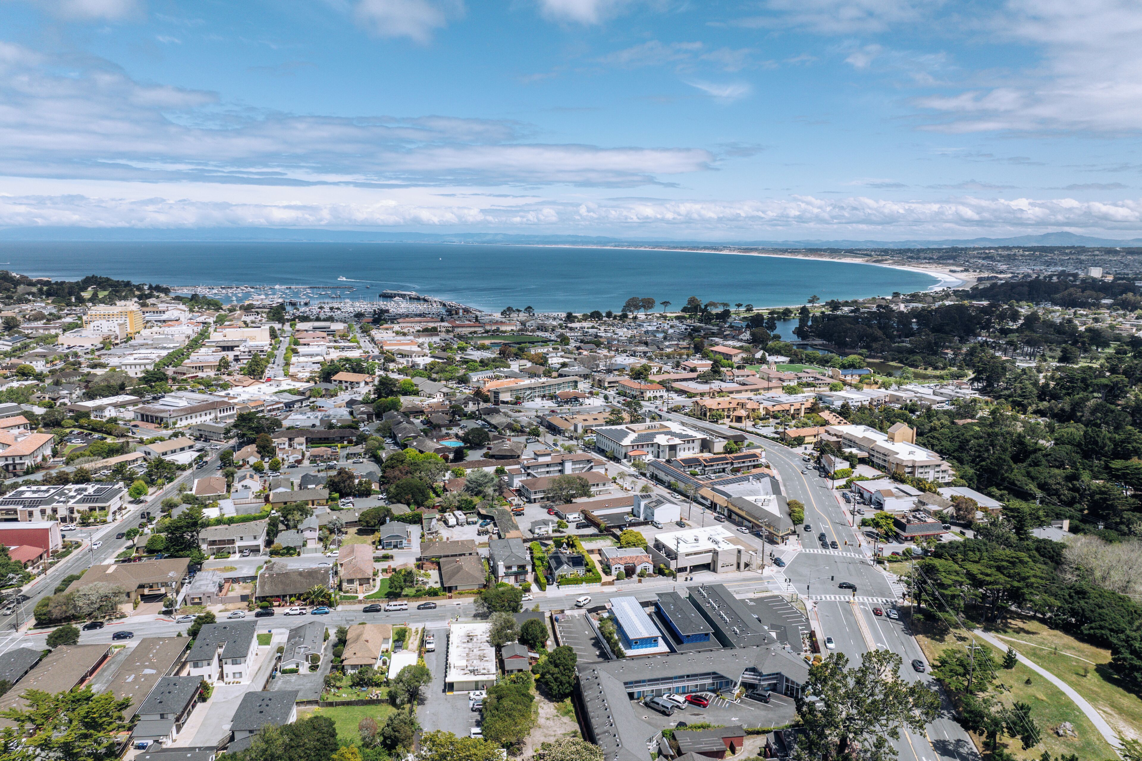 A coastal town with a mix of residential and commercial buildings, a clear view of the ocean, and a road leading towards the beach.