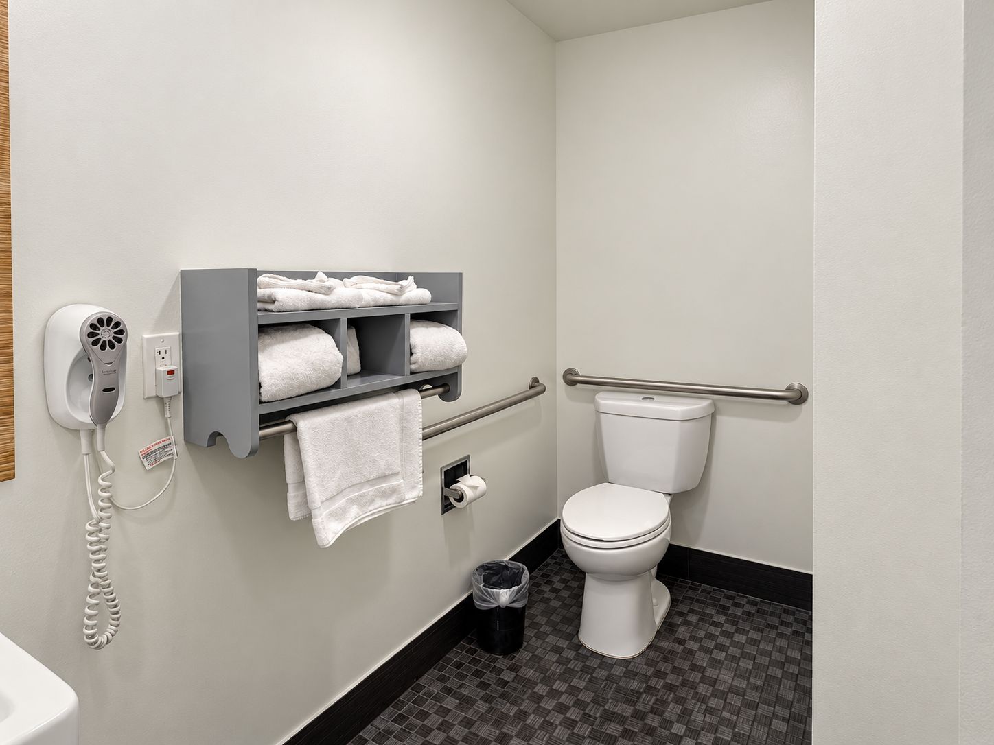 A bathroom with a toilet, a towel rack with towels, a hairdryer, and a trash can.