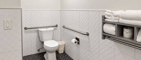 Een badkamer met toilet, handgrepen, een handdoekhouder en een prullenbak.