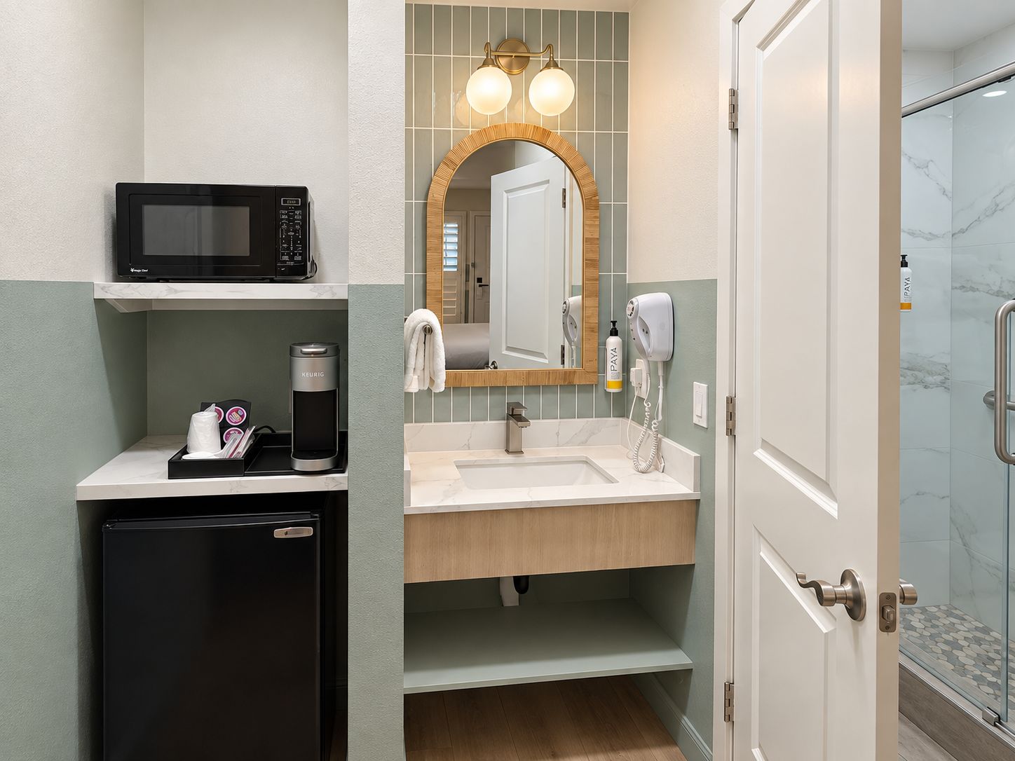 Un baño de hotel pequeño con microondas, cafetera y secador de pelo sobre la encimera.