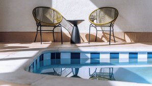 A poolside area with two wicker chairs and a small table, surrounded by a tiled deck.