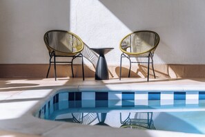 A poolside area with two wicker chairs and a small table, surrounded by a tiled deck.