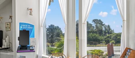Un comptoir d’enregistrement, deux fauteuils en osier avec des coussins, une petite table et une vue sur la verdure grâce à de grandes fenêtres.