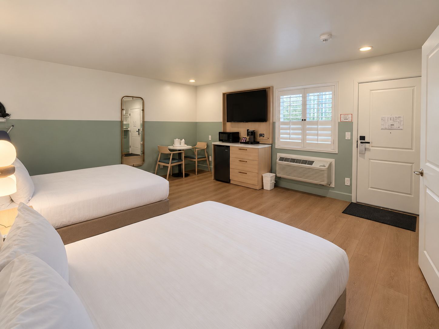 A hotel room with two beds, a desk with a chair, a television, and a window with blinds.