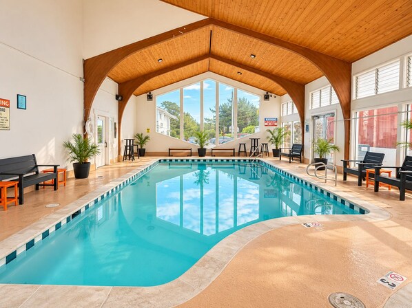 An indoor swimming pool with a wooden ceiling, large windows, and seating areas. -  Stargazer Hotel (Monterey)