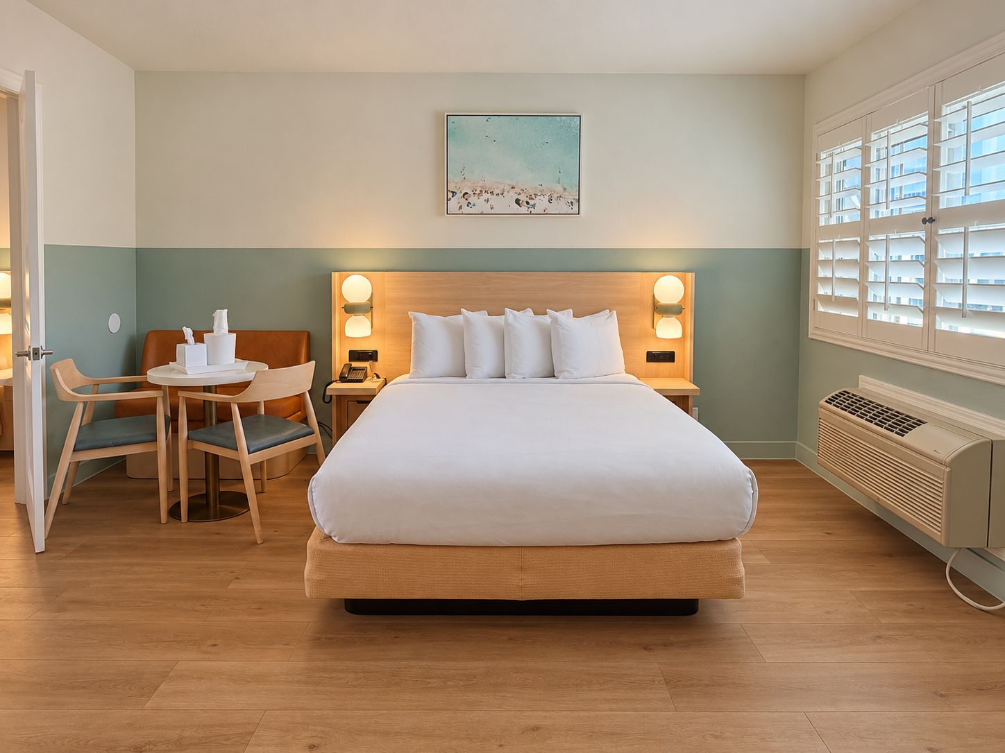 A hotel room with a large bed, a desk with chairs, a painting on the wall, and a window with blinds.