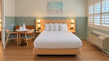 Une chambre d’hôtel avec un grand lit, un bureau avec des chaises, un tableau au mur et une fenêtre avec des stores.