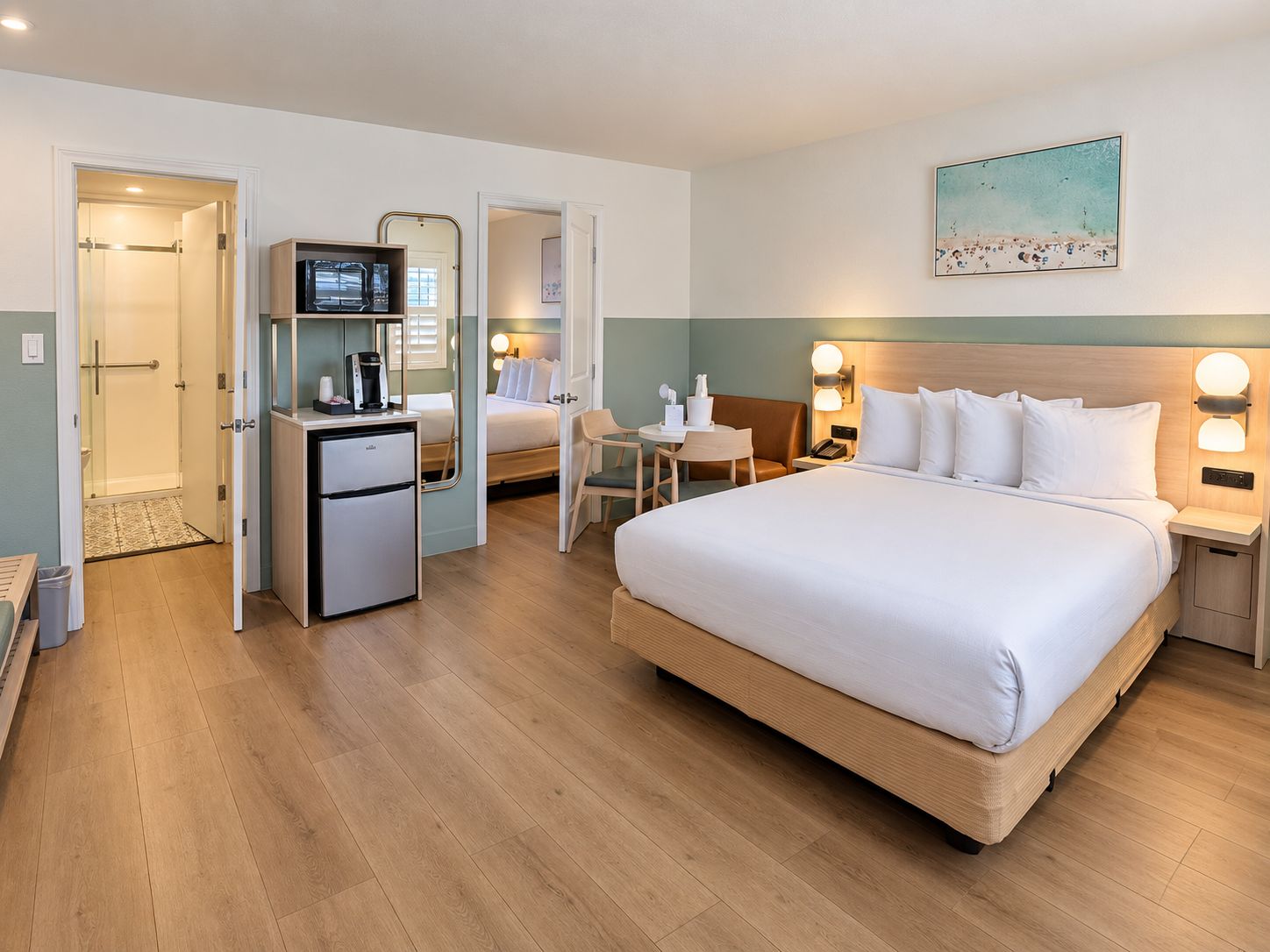 A hotel room with a bed, a desk, a refrigerator, a shower, and a painting on the wall.