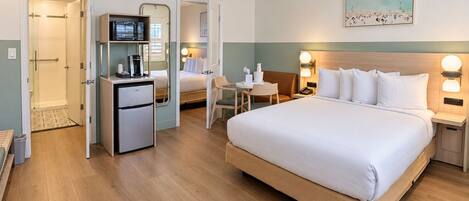 A hotel room with a bed, a desk, a refrigerator, a shower, and a painting on the wall.