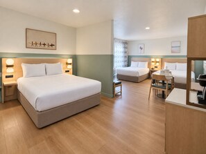 A hotel room with a large bed, a smaller bed, a desk, and a chair. There are wall-mounted lights and a painting on the wall. -  Stargazer Hotel (Monterey)