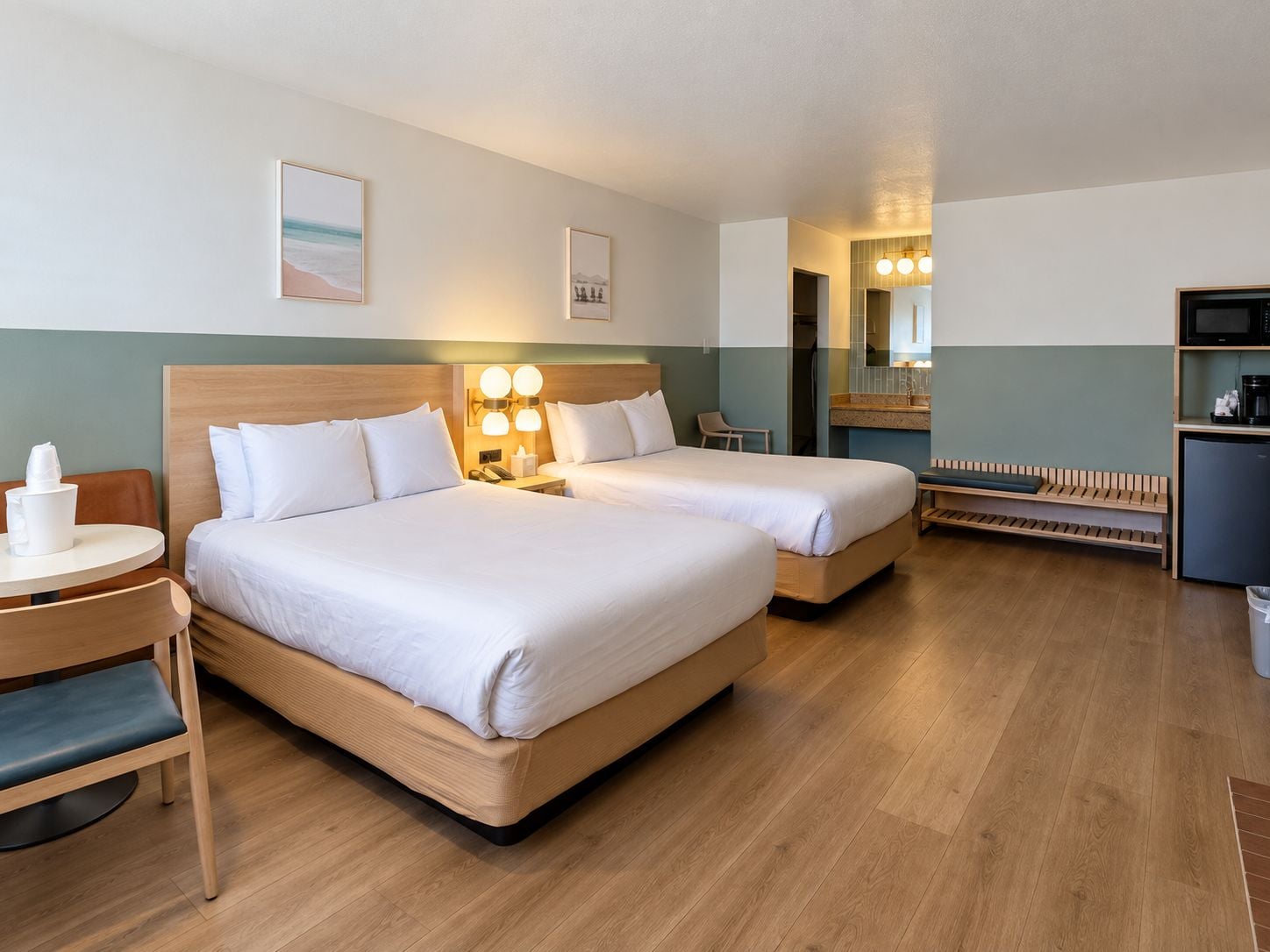 A hotel room with two beds, a desk, a chair, a small table, a microwave, and a trash bin.