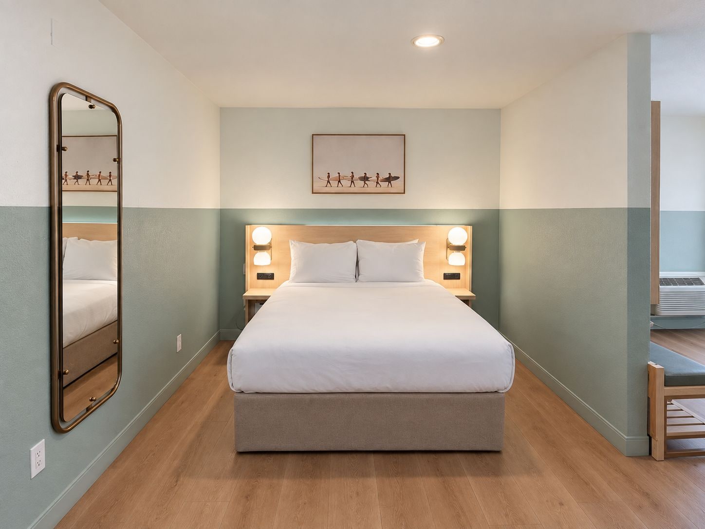 A hotel room with a bed, bedside lamps, a wall-mounted mirror, and a framed picture above the bed.