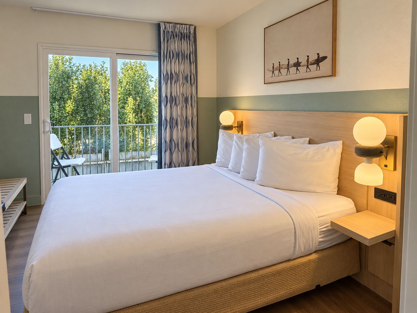 Habitació d'hotel amb un llit gran, un balcó amb una cadira i un quadre a la paret.