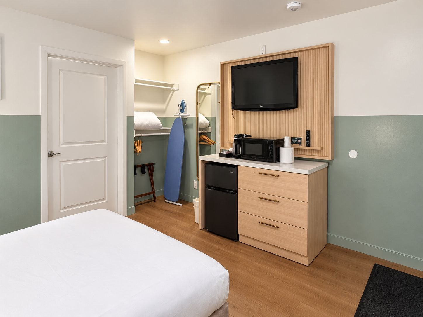 Una habitación de hotel con una cama, una kitchenette pequeña con microondas, un televisor y un armario de madera.