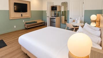 Une chambre d’hôtel comprenant un lit, un téléviseur fixé au mur, une petite kitchenette, un coin salon et un miroir.