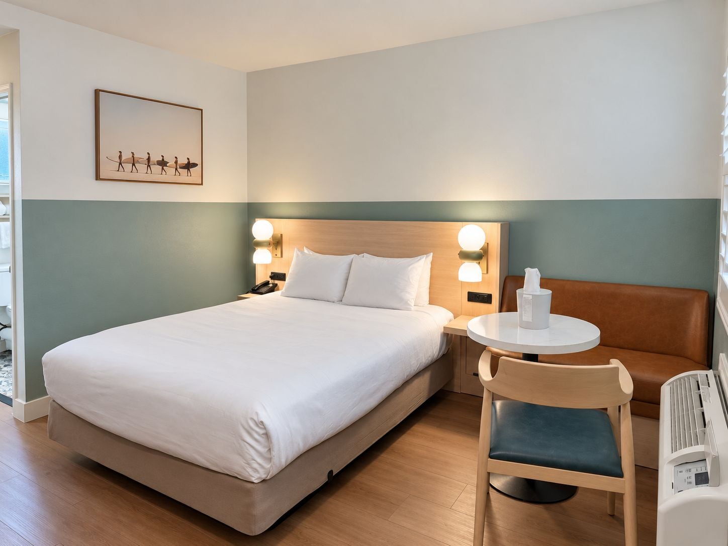 Habitación de hotel con cama, mesitas de noche, una silla, una pequeña mesa y un cuadro colgado en la pared.