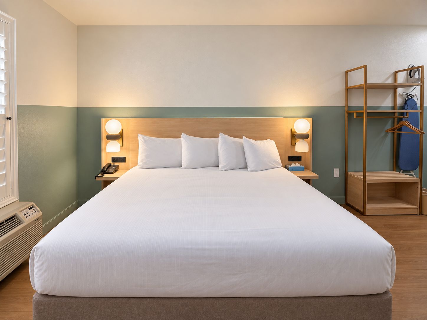 Ein Hotelzimmer mit einem großen Bett, Nachttischlampen, einem hölzernen Kopfteil, einem Nachttisch mit Telefon und einem Kleiderschrank mit Kleiderstange.