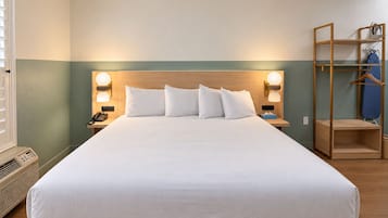 Habitación de hotel con una cama grande, lámparas de noche, un cabecero de madera, una mesita de noche con teléfono y un armario con perchero.