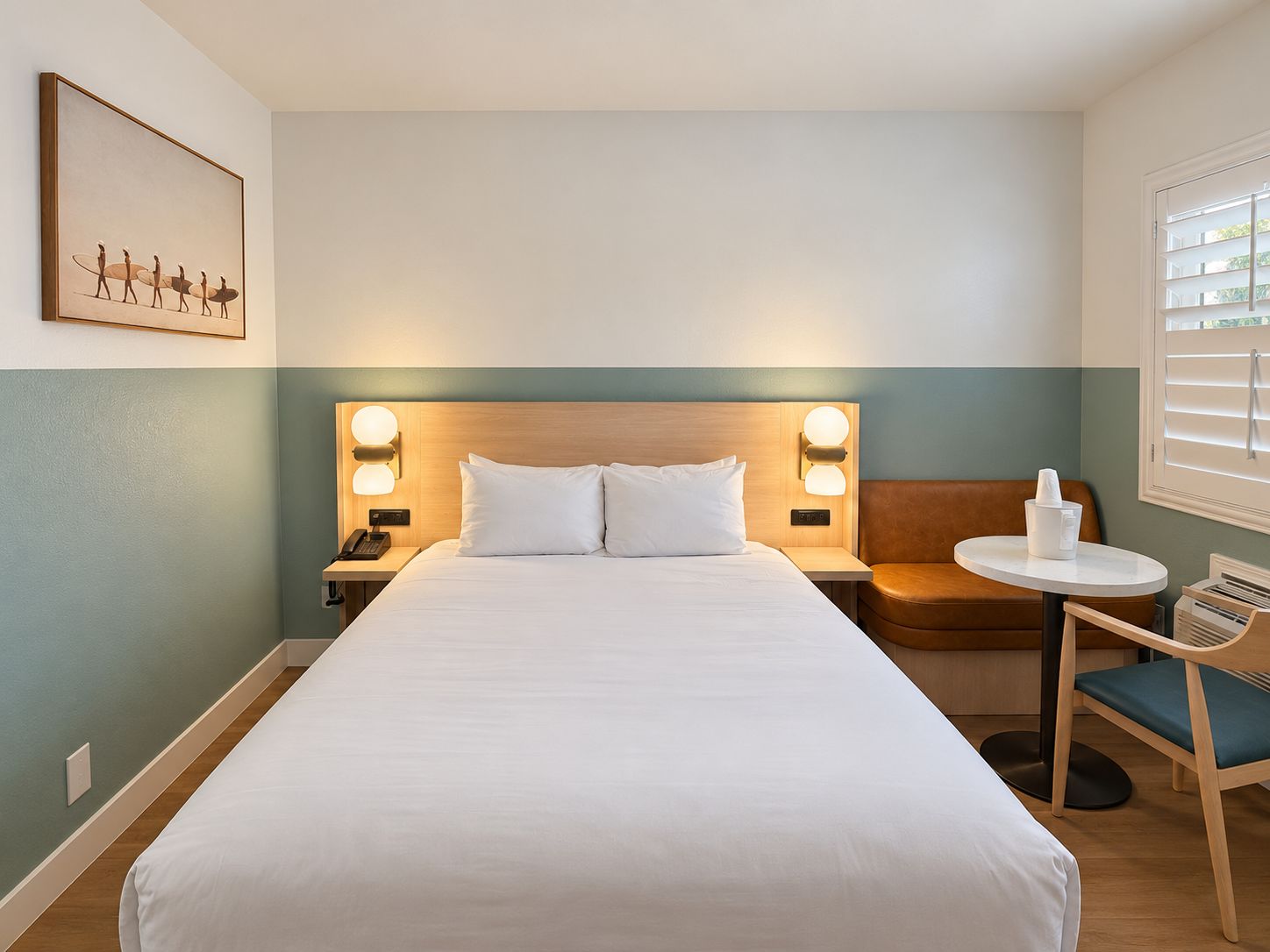 Una habitación de hotel con cama, mesitas de noche, una silla y una pequeña mesa.