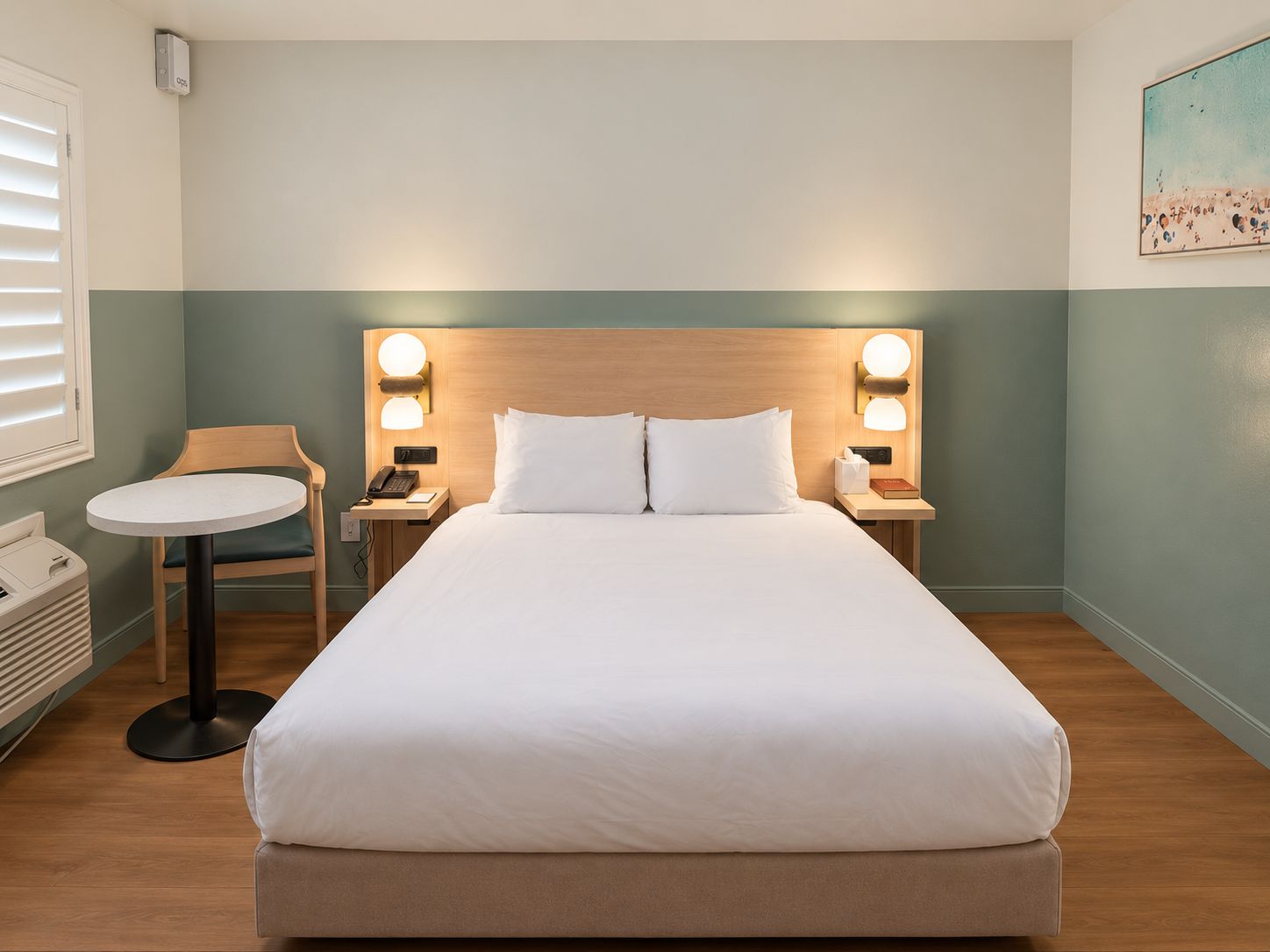 A hotel room with a bed, bedside tables, a chair, and a small table.