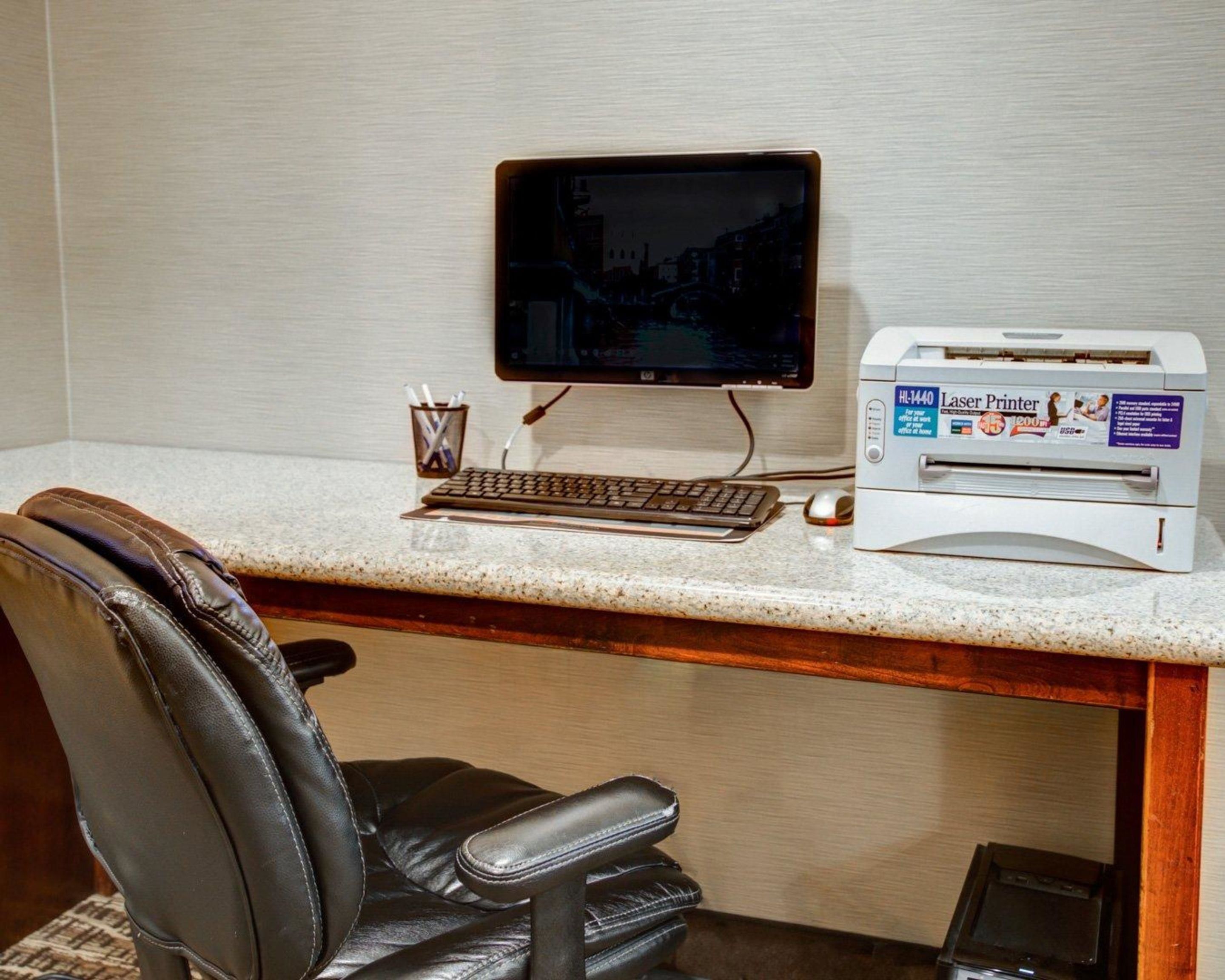 A hotel workspace with a desktop computer, a monitor, a keyboard, a mouse, and a laser printer.