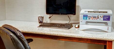 A hotel workspace with a desktop computer, a monitor, a keyboard, a mouse, and a laser printer.