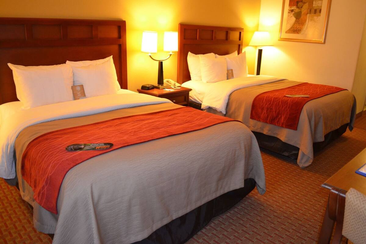 A hotel room with two beds, each with a red blanket, a nightstand with a lamp, and a telephone.