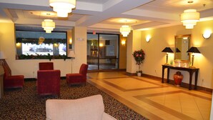 A lobby with red chairs, a white sofa, a patterned carpet, and a large window with a view of a parking lot.