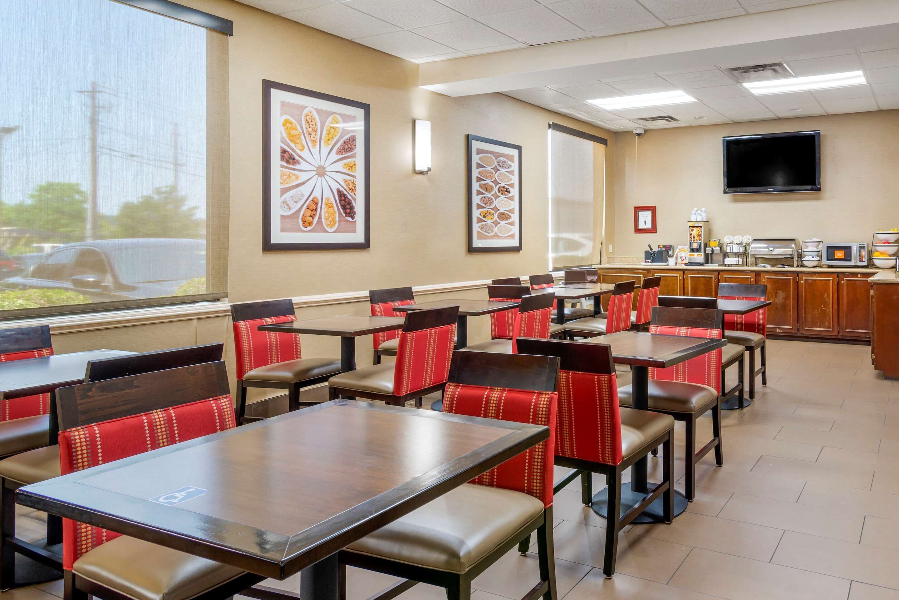 A restaurant with multiple tables and chairs, a counter with a cash register, and framed pictures on the wall.