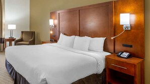 A hotel room with a large bed, a wooden headboard, bedside lamps, a chair, and a nightstand with a phone. - Comfort Inn Columbus near Fort Benning (Columbus)