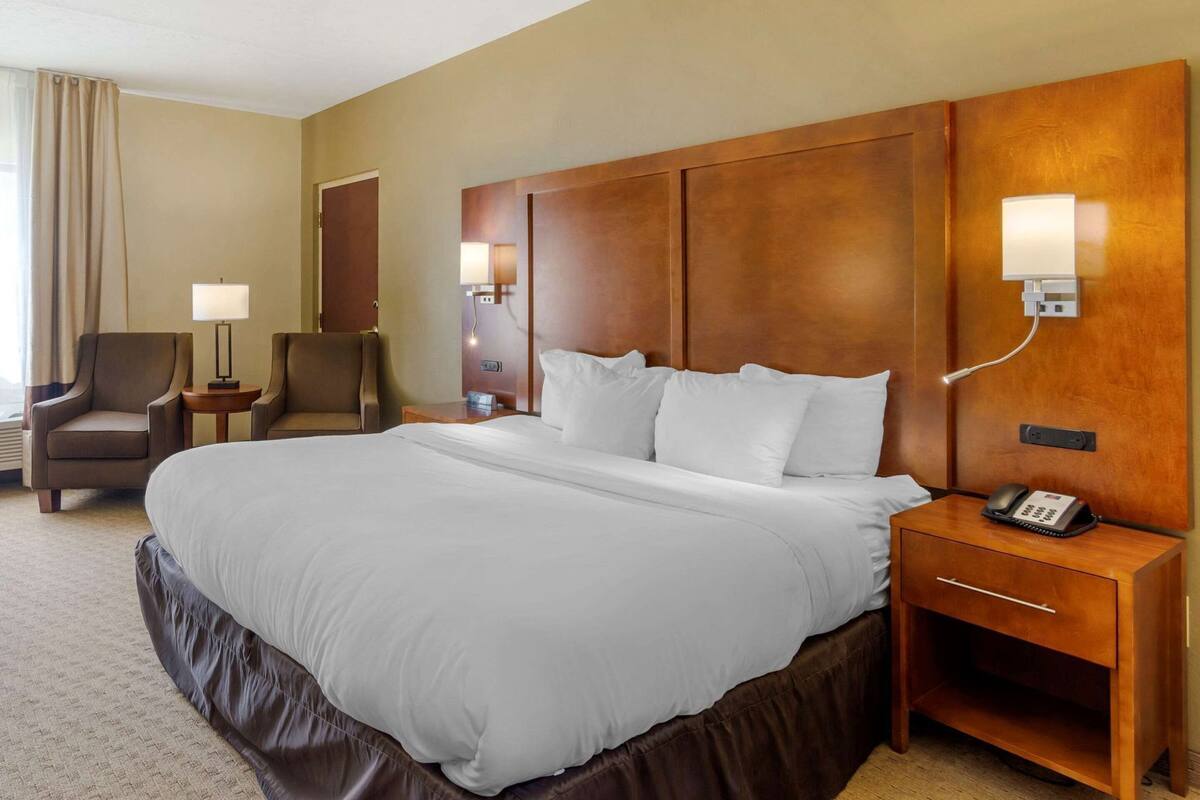 A hotel room with a large bed, a desk with a phone, a chair, and a lamp.