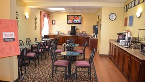 A breakfast area with tables and chairs, a coffee station, and a television on the wall.