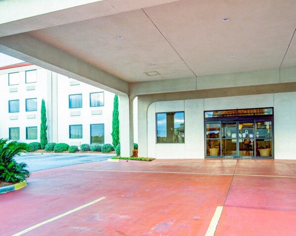 A modern hotel entrance with a covered walkway, a glass door entrance, and a parking area.