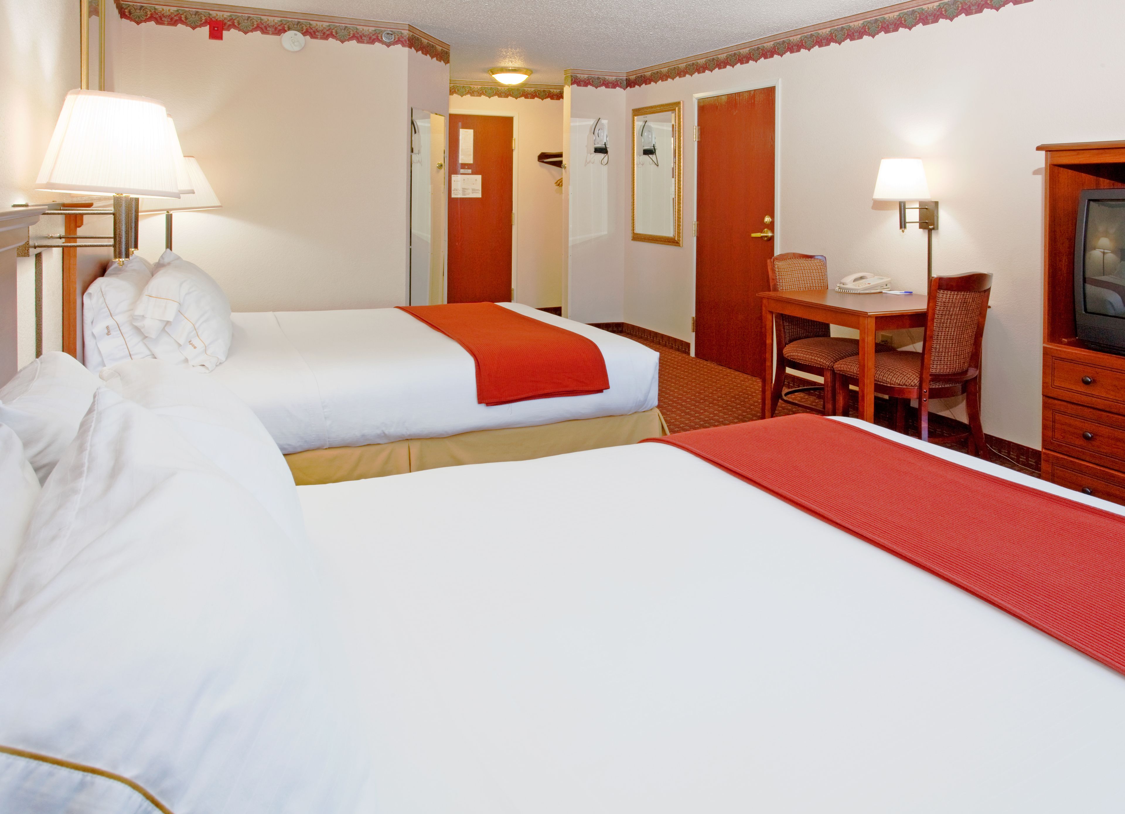 A hotel room with two beds, a desk with a chair, a television, and a lamp.