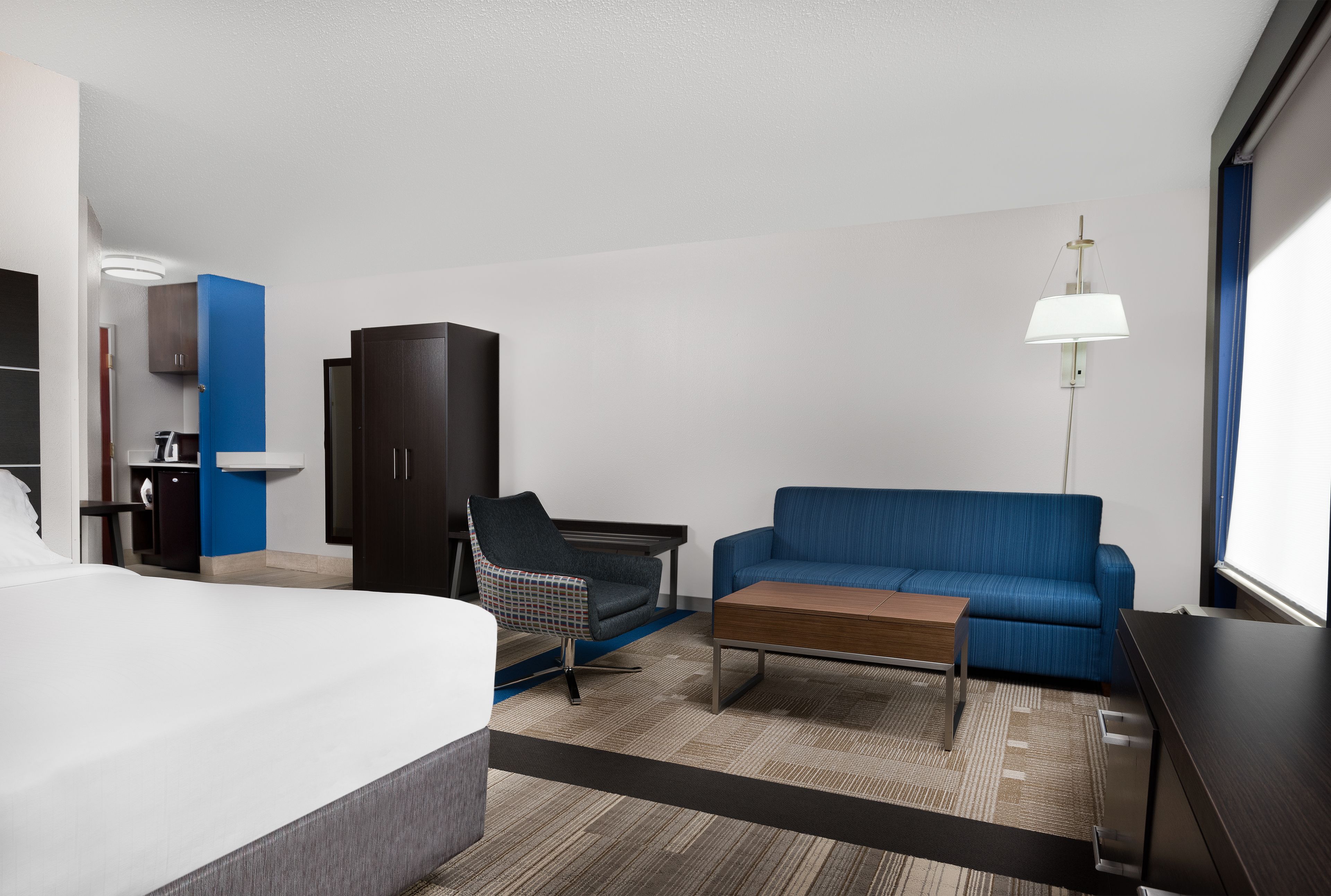 Habitación de hotel con cama, sofá azul, escritorio, silla, armario y lámpara.