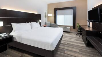 Habitación de hotel con una cama grande, un escritorio con computadora, televisor y ventana con persianas.