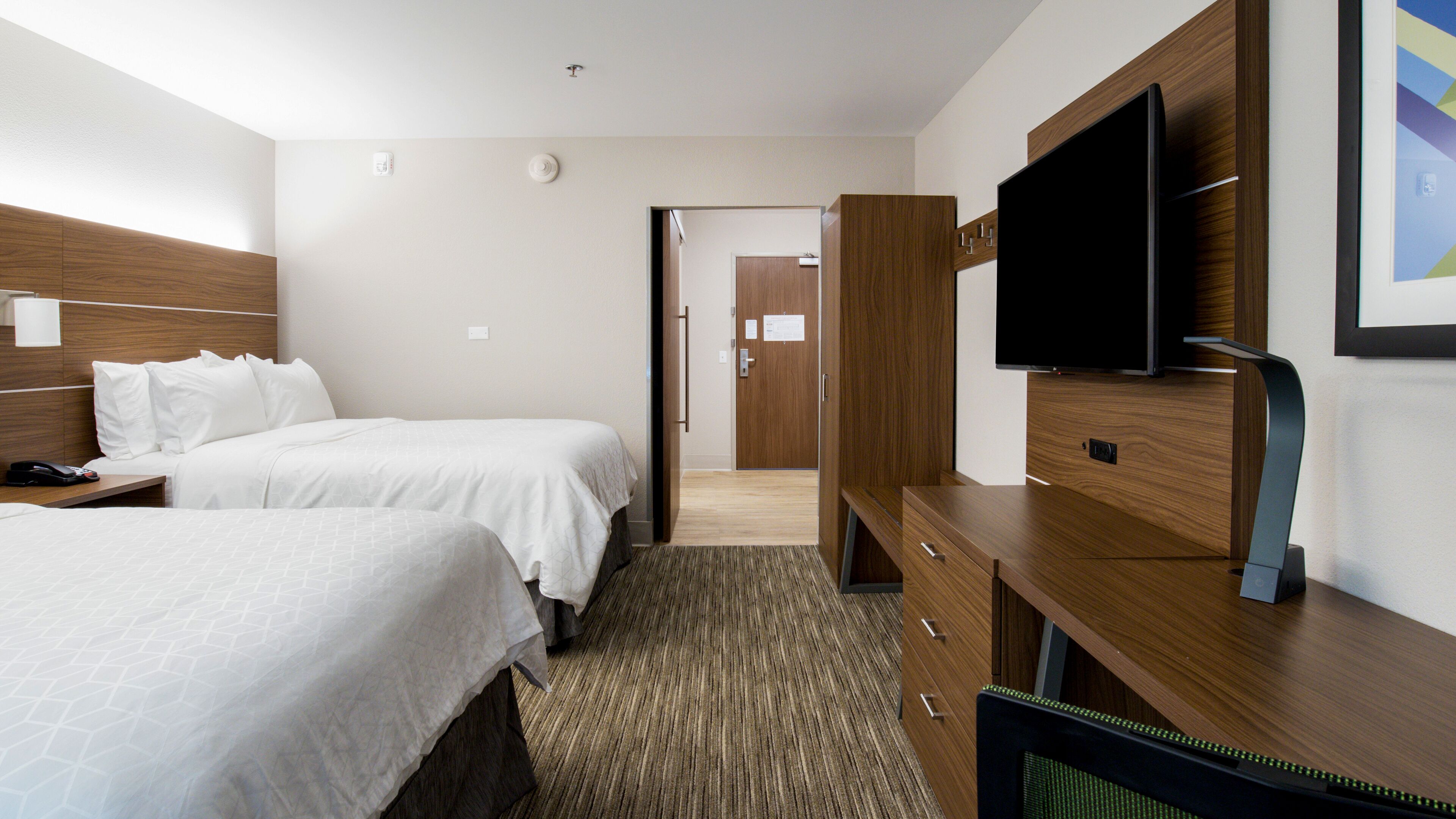 Ein Hotelzimmer mit zwei Betten, einem Fernseher, einem Schreibtisch und einer Tür zu einem weiteren Raum.
