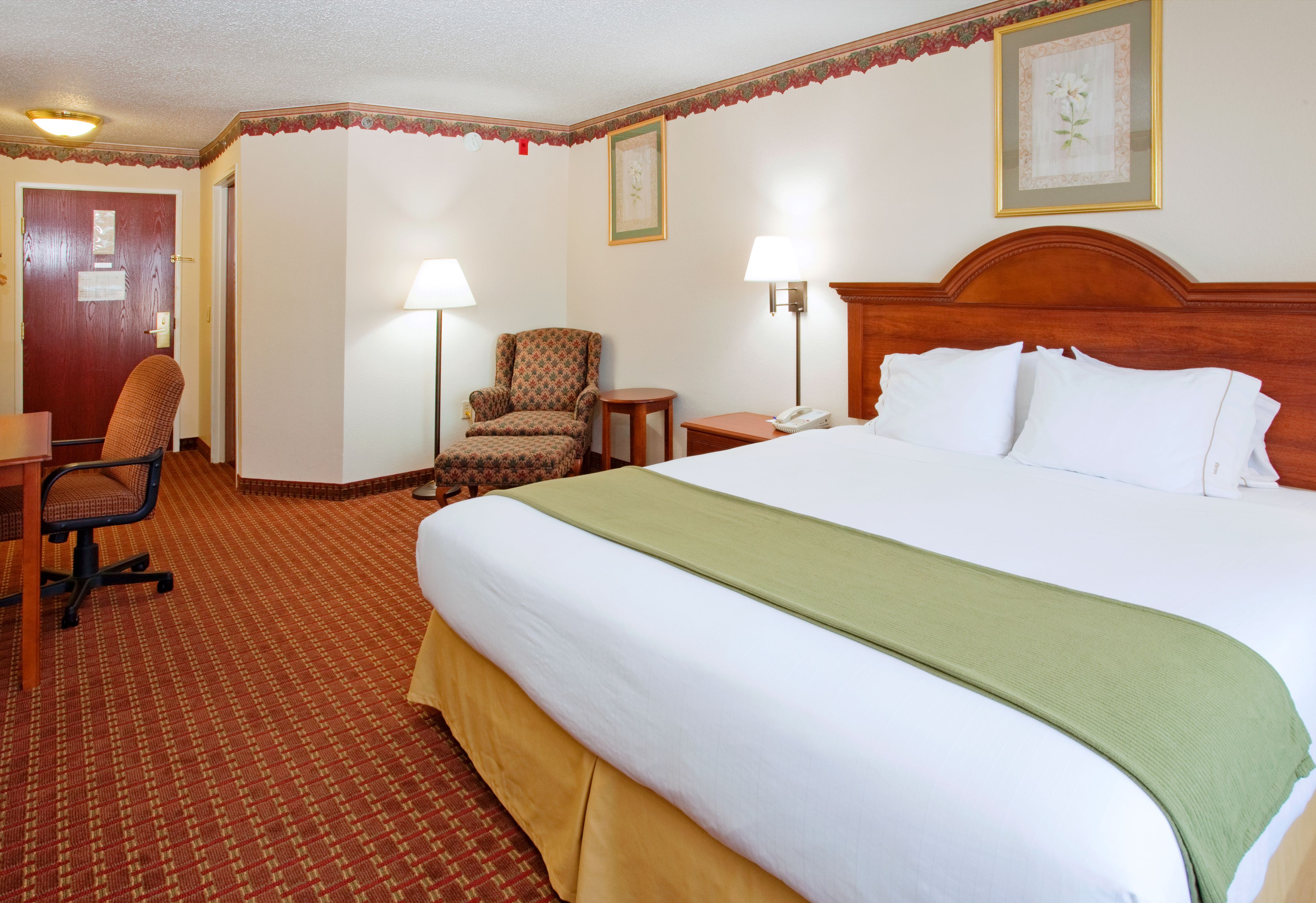 A hotel room with a large bed, a chair, a desk, and two lamps.