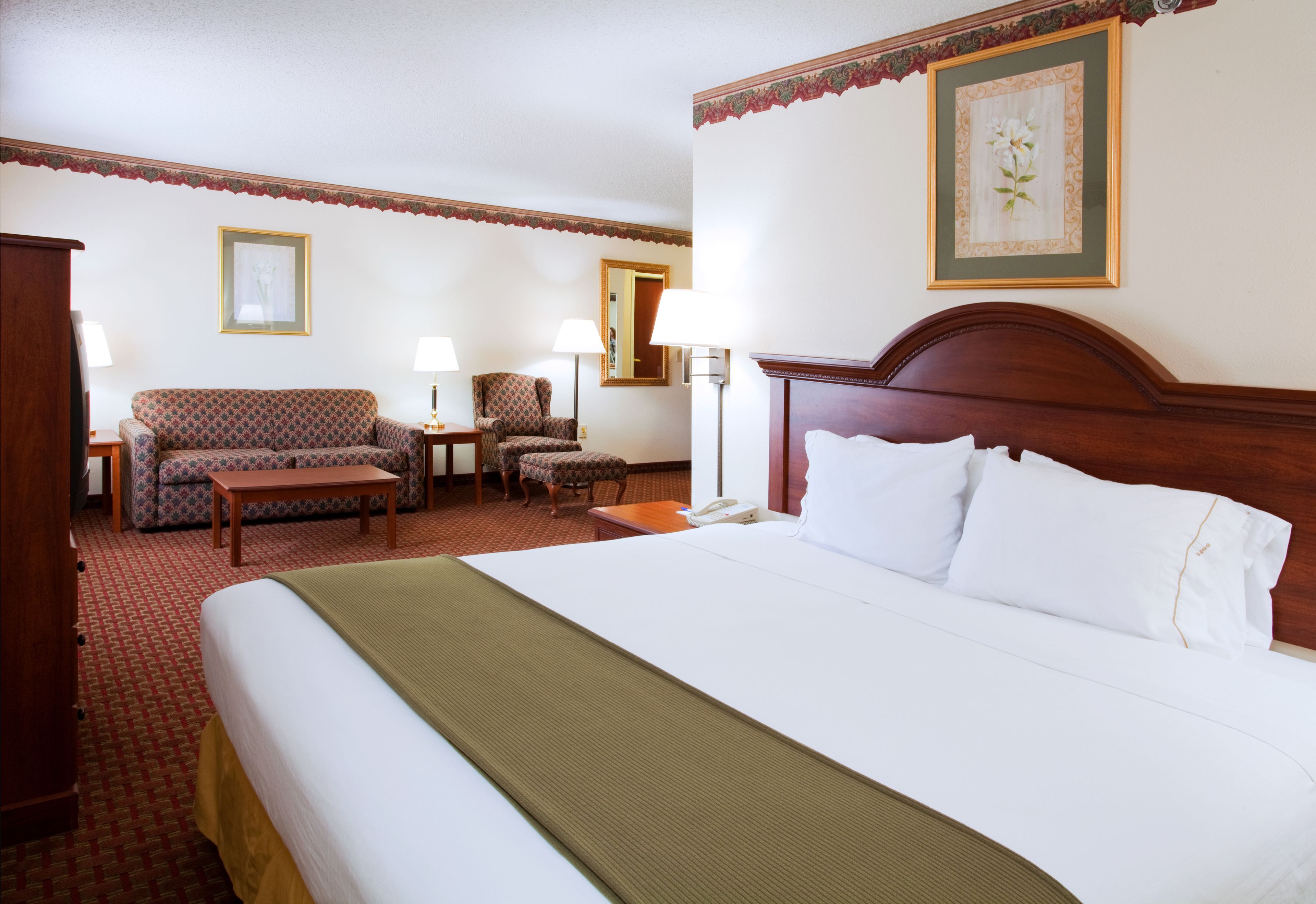 A hotel room with a large bed, a sofa, a chair, a desk, and a lamp.