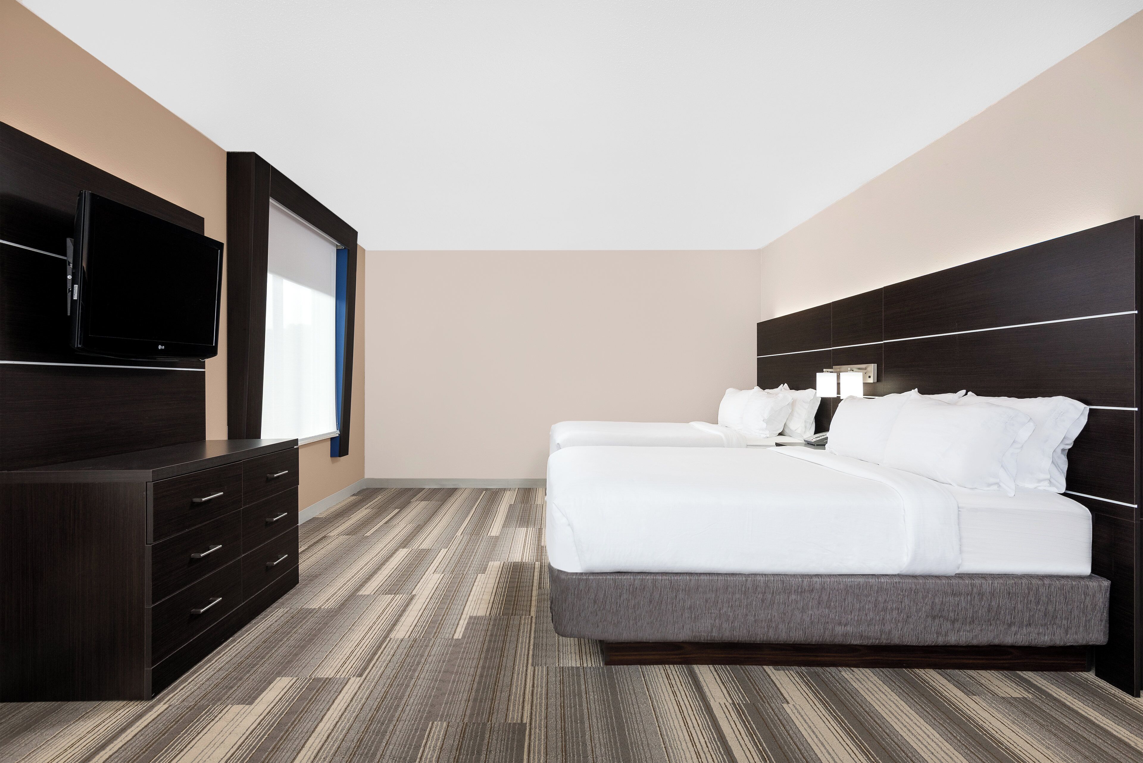 Ein Hotelzimmer mit einem Bett, einem Fernseher, einer Kommode und einem gemusterten Teppich.