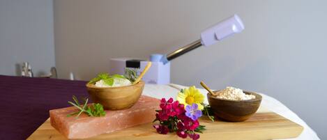 A wooden board with a salmon fillet, a bowl of herbs, and a knife on a bed with a purple bedspread.