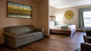 Una habitación de hotel con un sofá a rayas, una cama con cabecera decorativa, un cuadro grande en la pared y una lámpara con forma de sol.