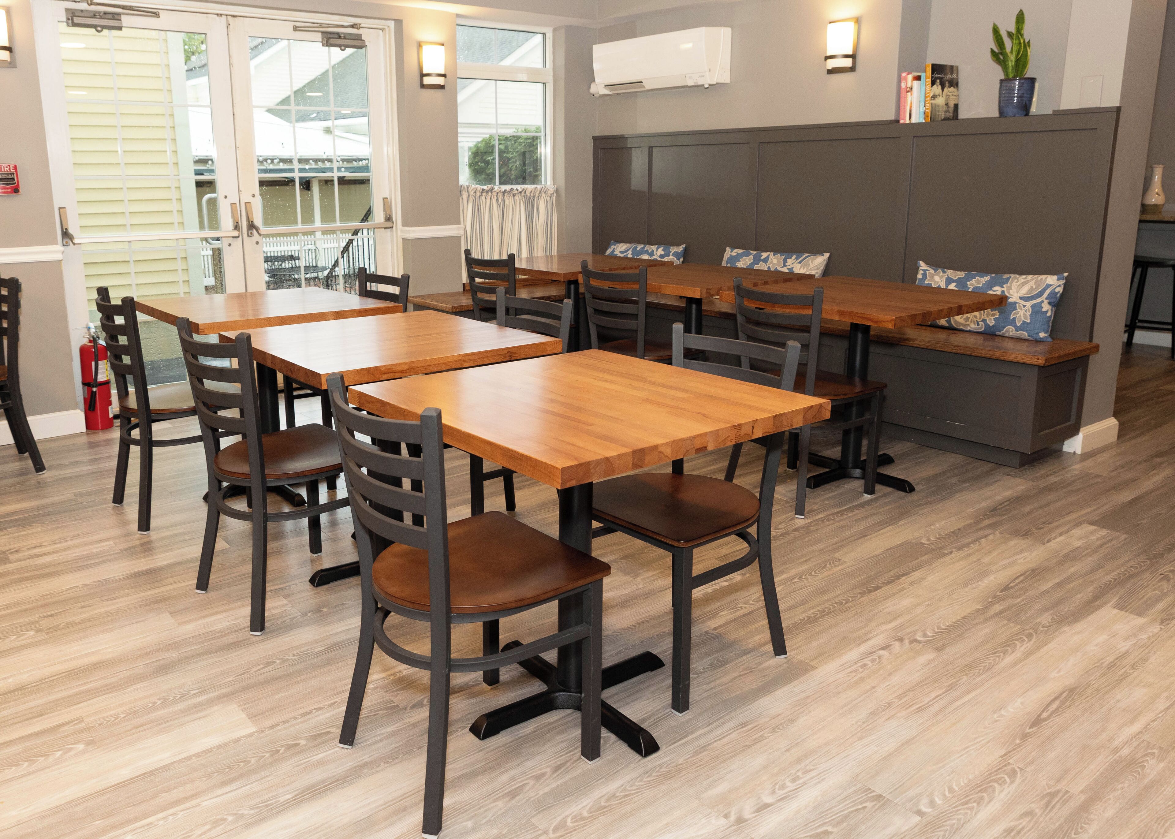 A dining area with wooden tables and chairs, a bench, and a view of the outside.