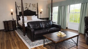 Un dormitorio con cama con dosel, un sofá de cuero, una mesa de centro de madera y vistas al verdor por la ventana.