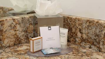 Un meuble-lavabo avec un dessus en marbre, une boîte de mouchoirs, un savon, une lotion pour le corps et un paquet de lingettes.